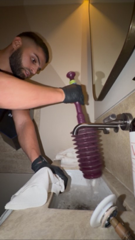 Plumber clearing a blocked bathroom basin with a plunger