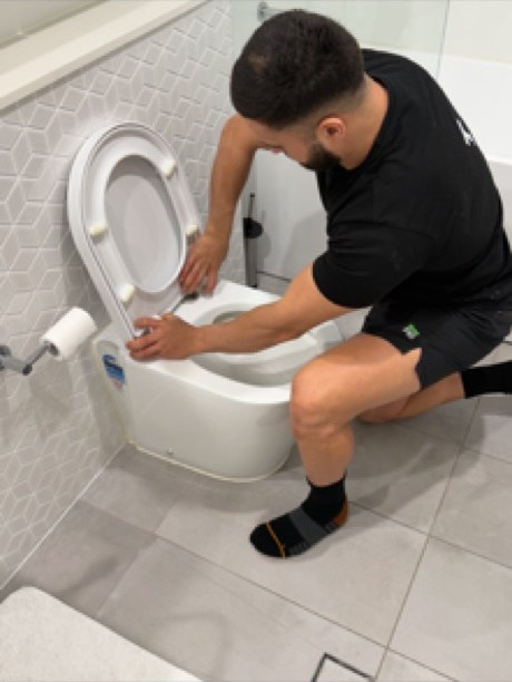 Plumber working on a wall-faced toilet in a tiled bathroom
