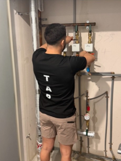 Plumber working on isolation valves above a bank of water meters